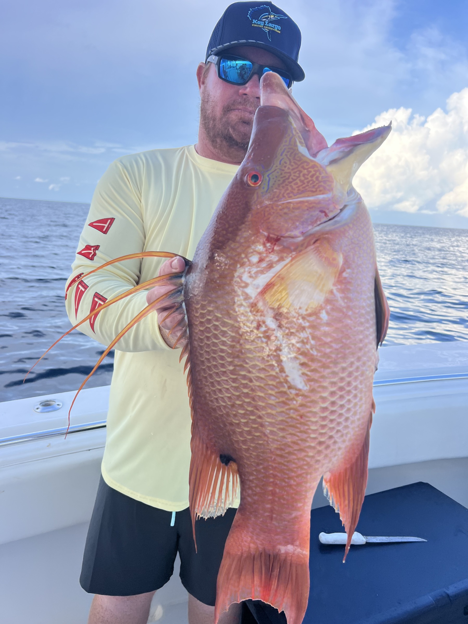 Angler holding a hogfish aboard a boat in a pale yellow custom shirt
