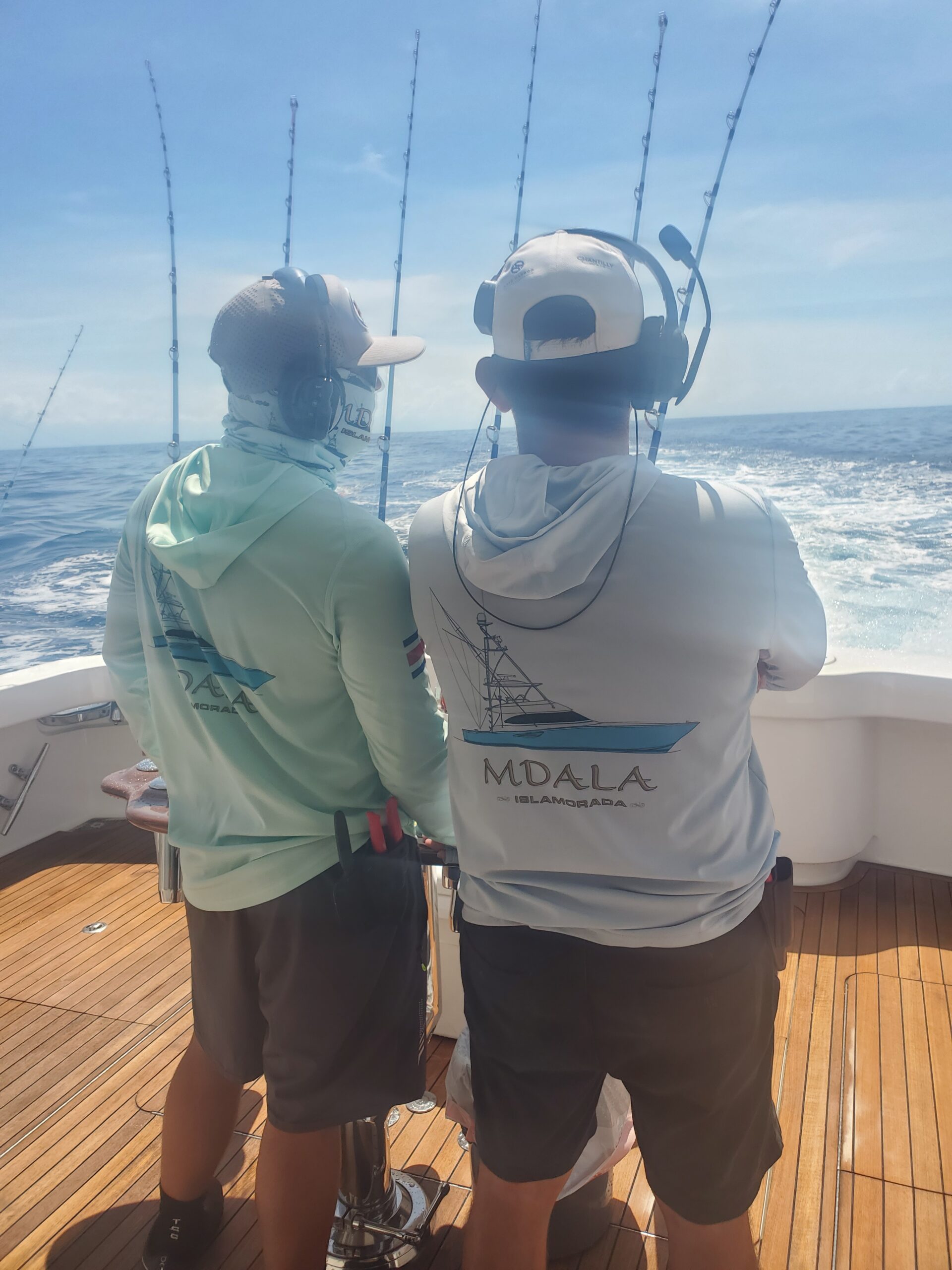 Two anglers wearing custom boat performance shirts aboard a sport-fishing boat